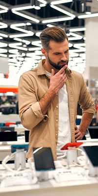 Mentality Shopperprofielen – Eigenwijze shoppers, jongeman met baard in een winkel die nadenkend met zijn hand aan zijn kin staat.
