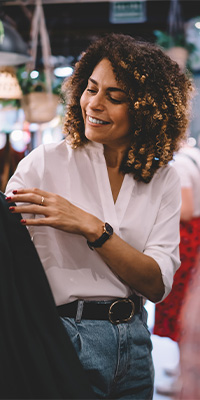 Mentality Shopperprofielen – Merkbewuste shoppers, jonge vrouw met krullen en wit overhemd die glimlachend naar haar telefoon kijkt.