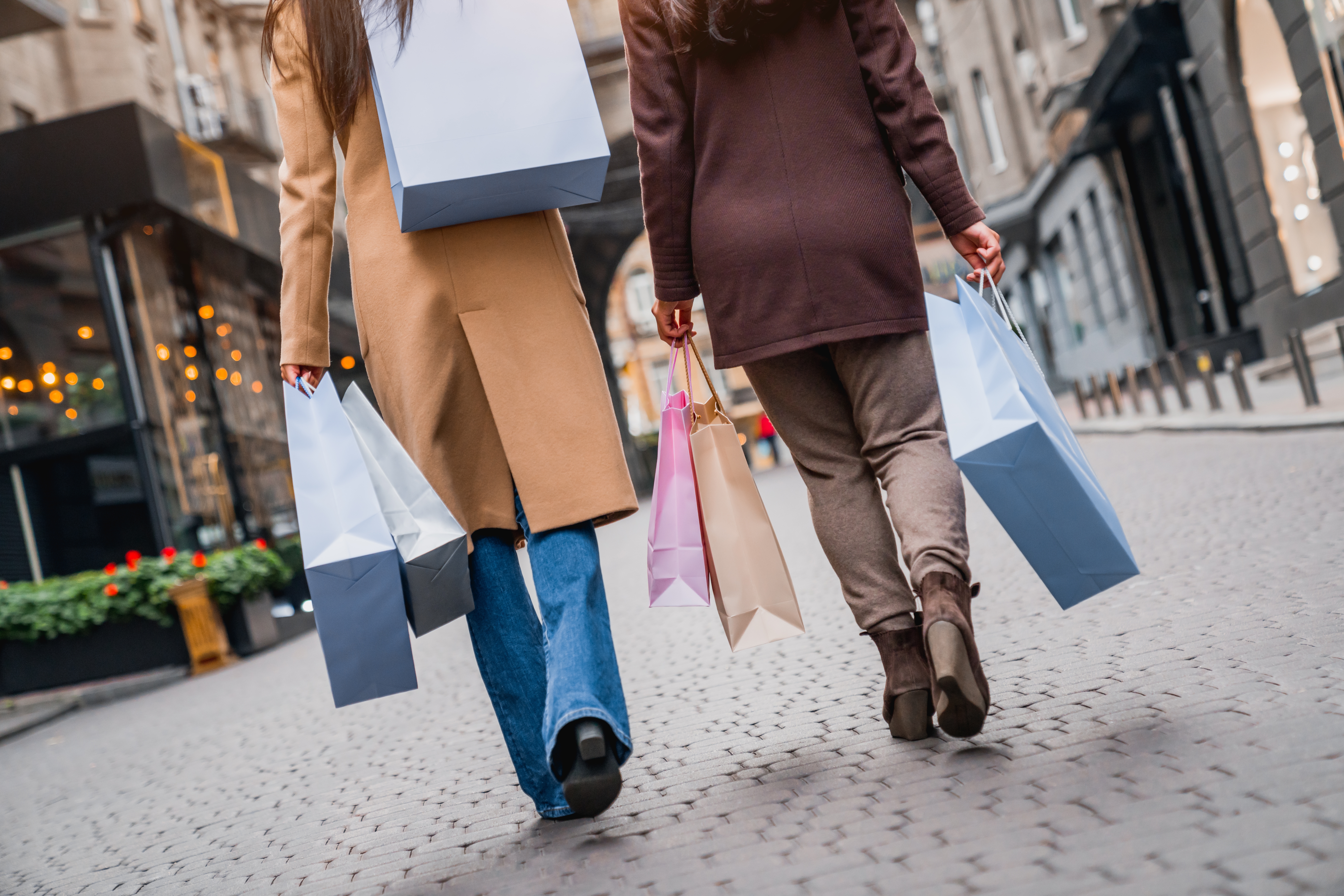 Twee mensen lopen met meerdere shoppingtassen door een winkelstraat.