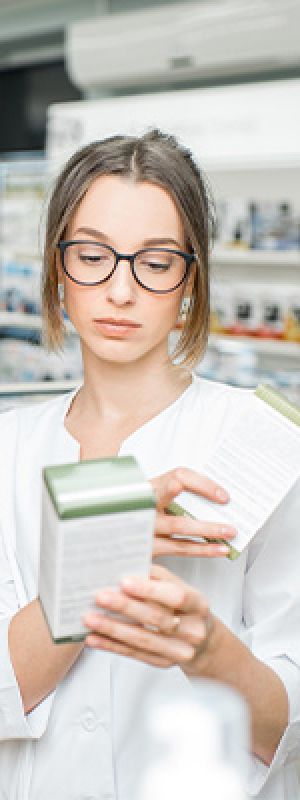 Mentality zorgprofielen – De pragmatische zorgcliënten, jonge vrouw met bril leest informatie op een verpakking in een apotheek.